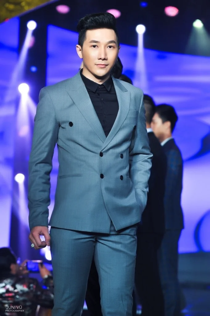 Người mẫu nam Phong mặc vest xám trình diễn trên sàn runway ánh đèn sân khấu