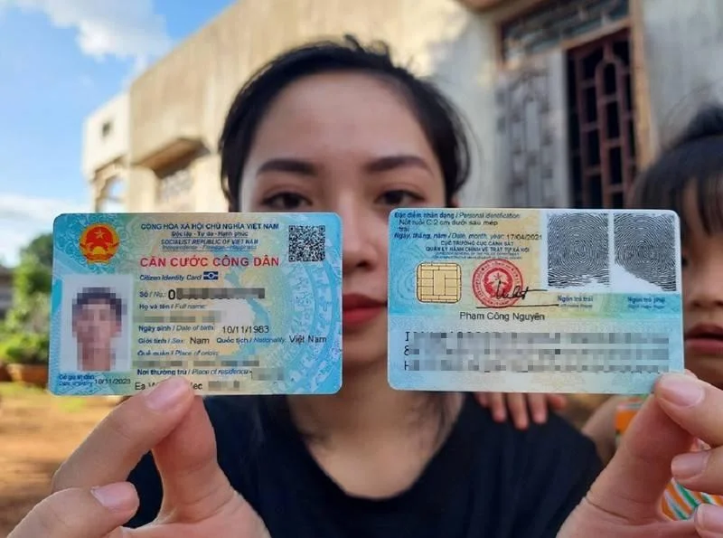 Ảnh CCCD giả - người phụ nữ cầm hai mặt căn cước công dân Việt Nam, thông tin cá nhân bị làm mờ, nền ngoài trời